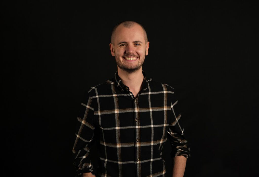 Image of smiling Joe Williams in check shirt in front of black background