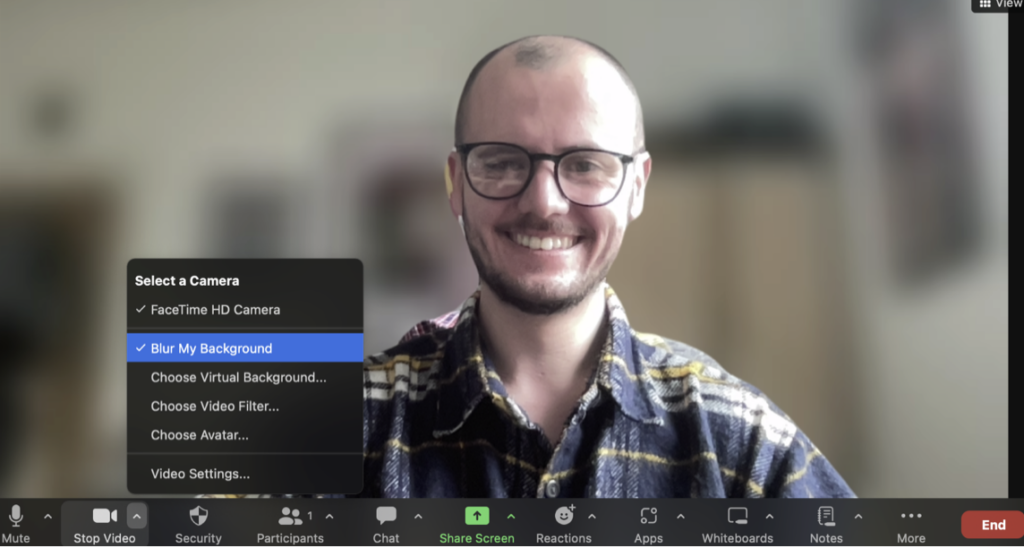 This is a screenshot of a Zoom video call with the background behind the participant blurred.